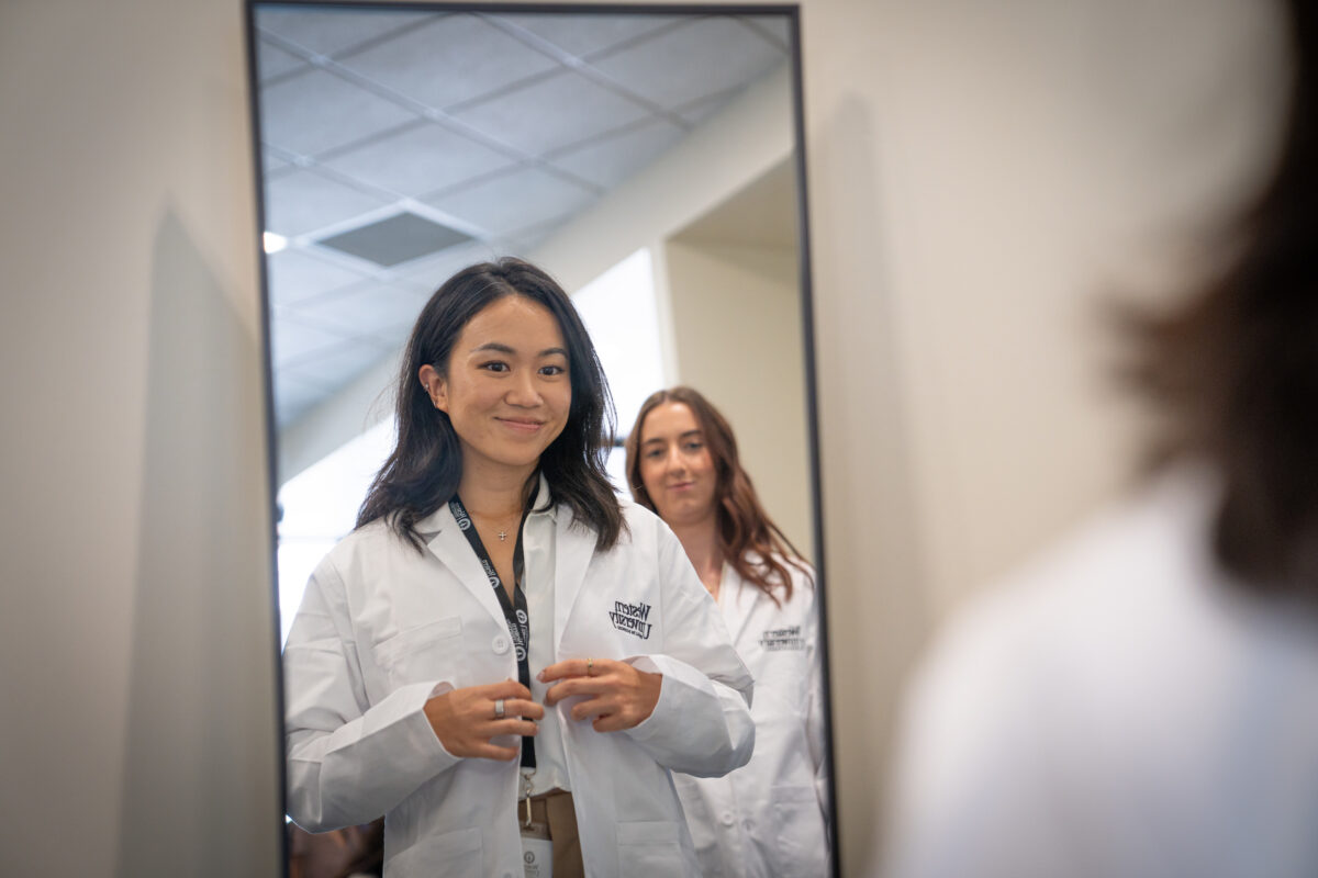 A woman in a lab coat looking at herself in the mirror.