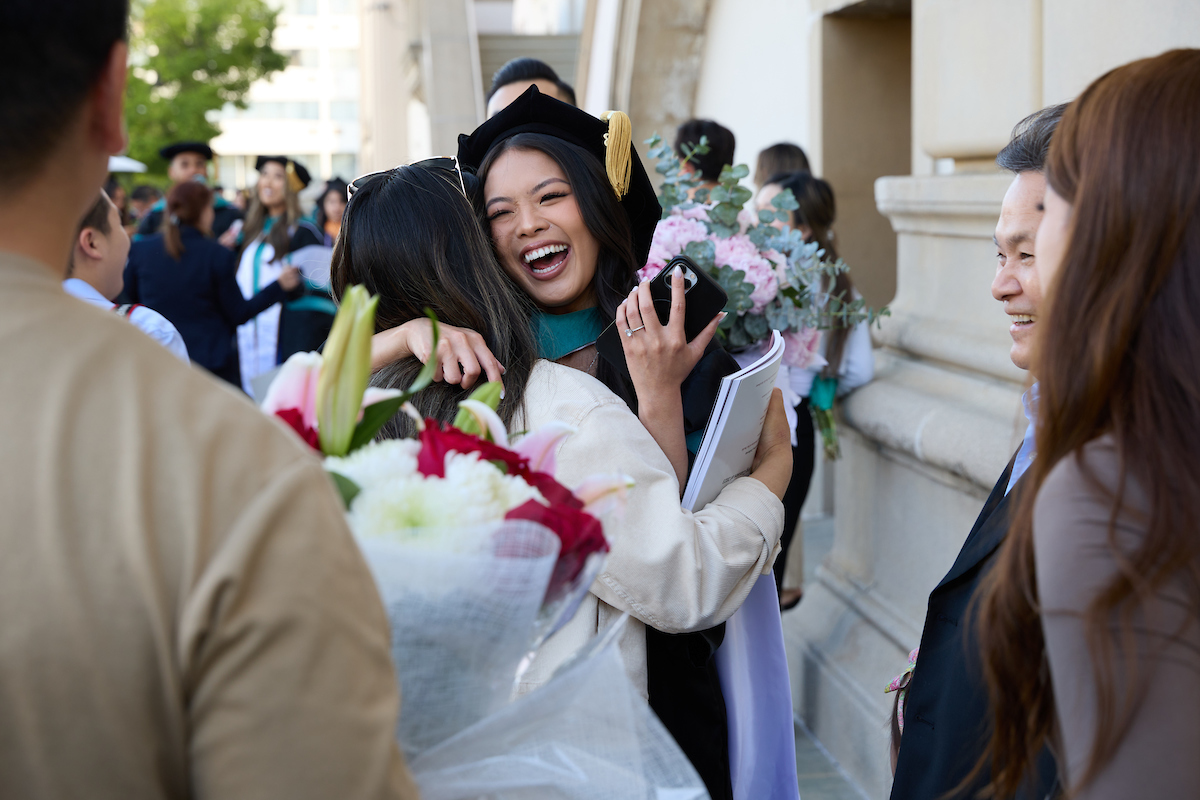 A woman in a graduation gown is hugging another woman.