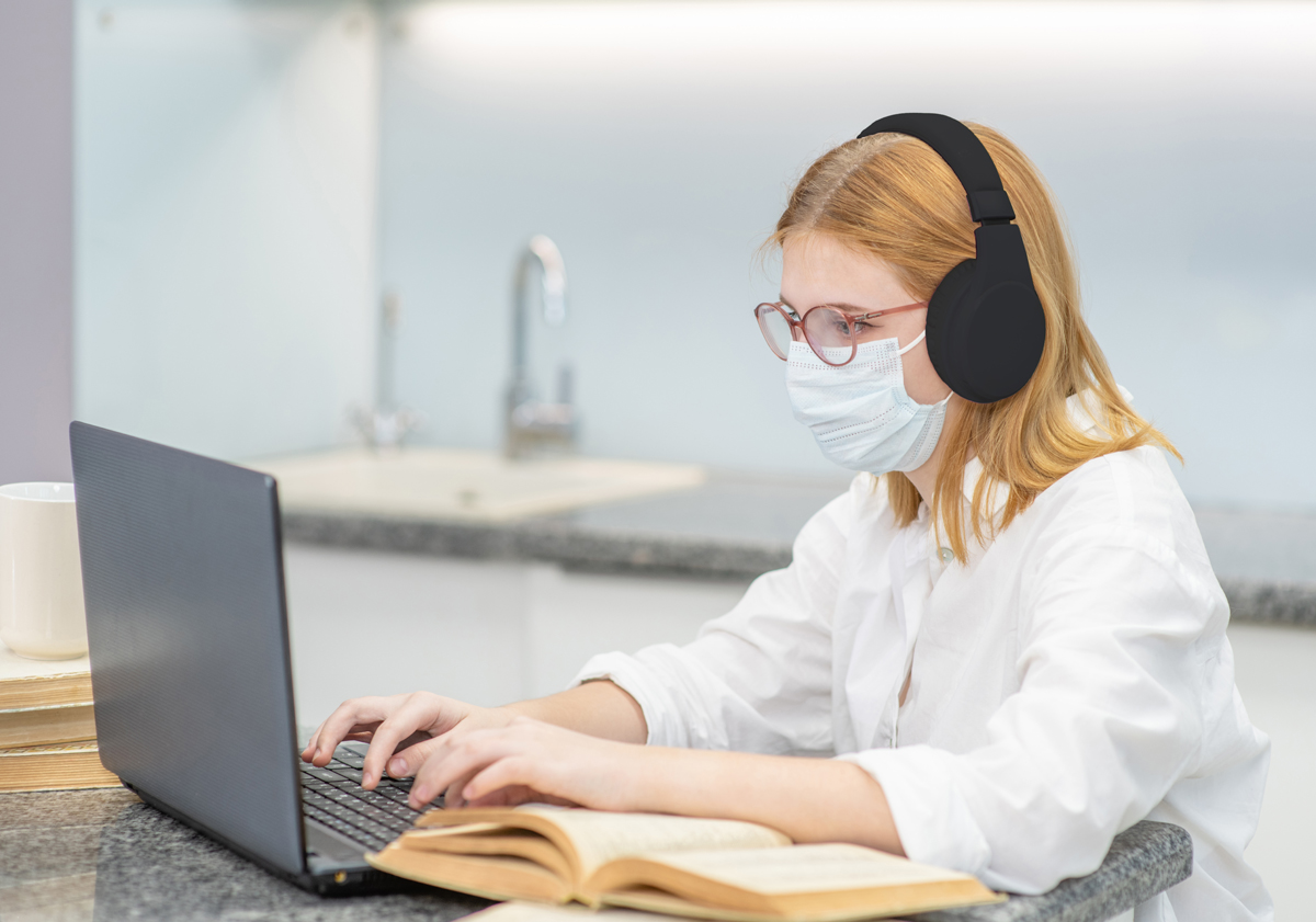 A woman wearing a face mask while using a laptop.