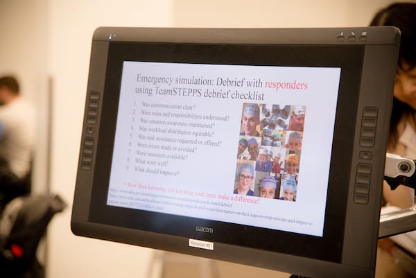 A computer screen displays an emergency simulation debrief checklist for responders, featuring a list of questions and a collage of people wearing surgical caps.