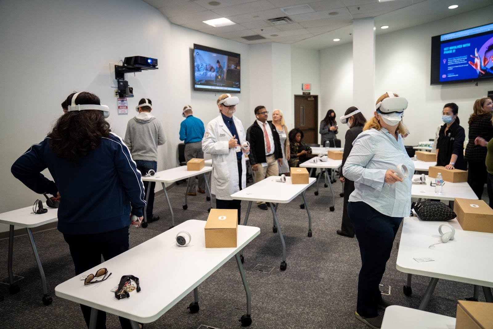 People in a room wearing VR headsets, surrounded by tables with brown boxes.