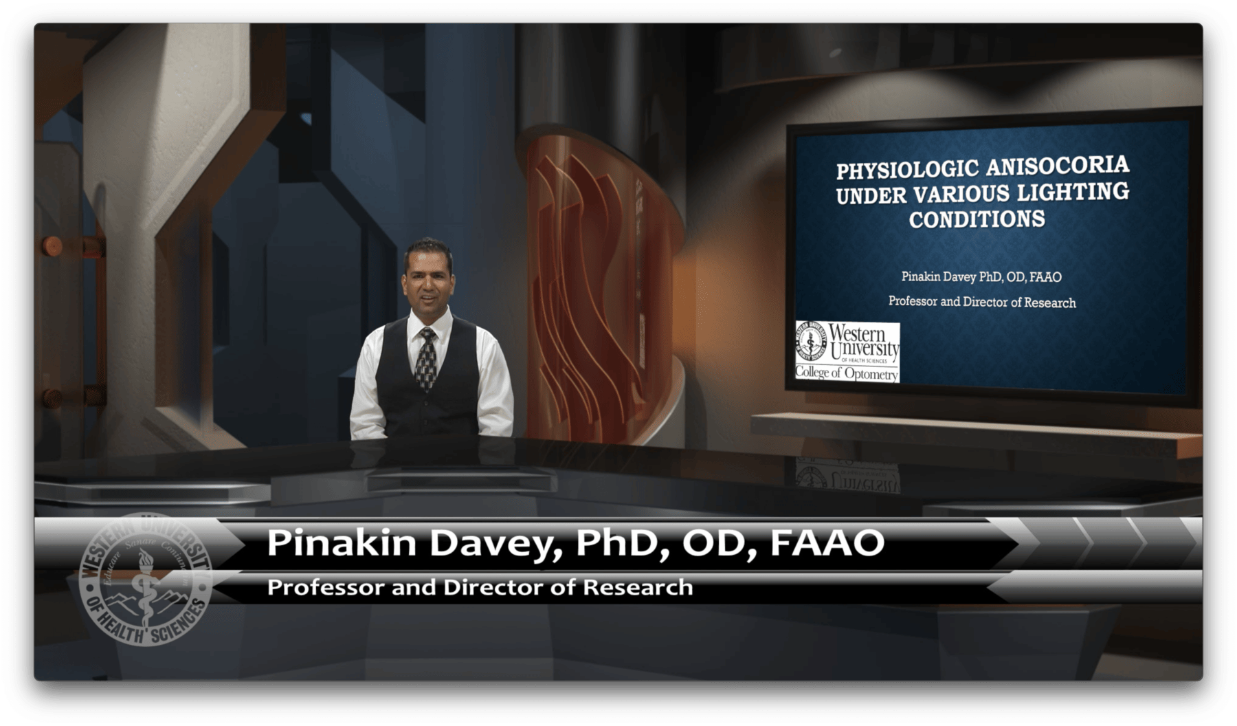 A man stands next to a presentation screen displaying a slide titled "Physiologic Anisocoria Under Various Lighting Conditions.
