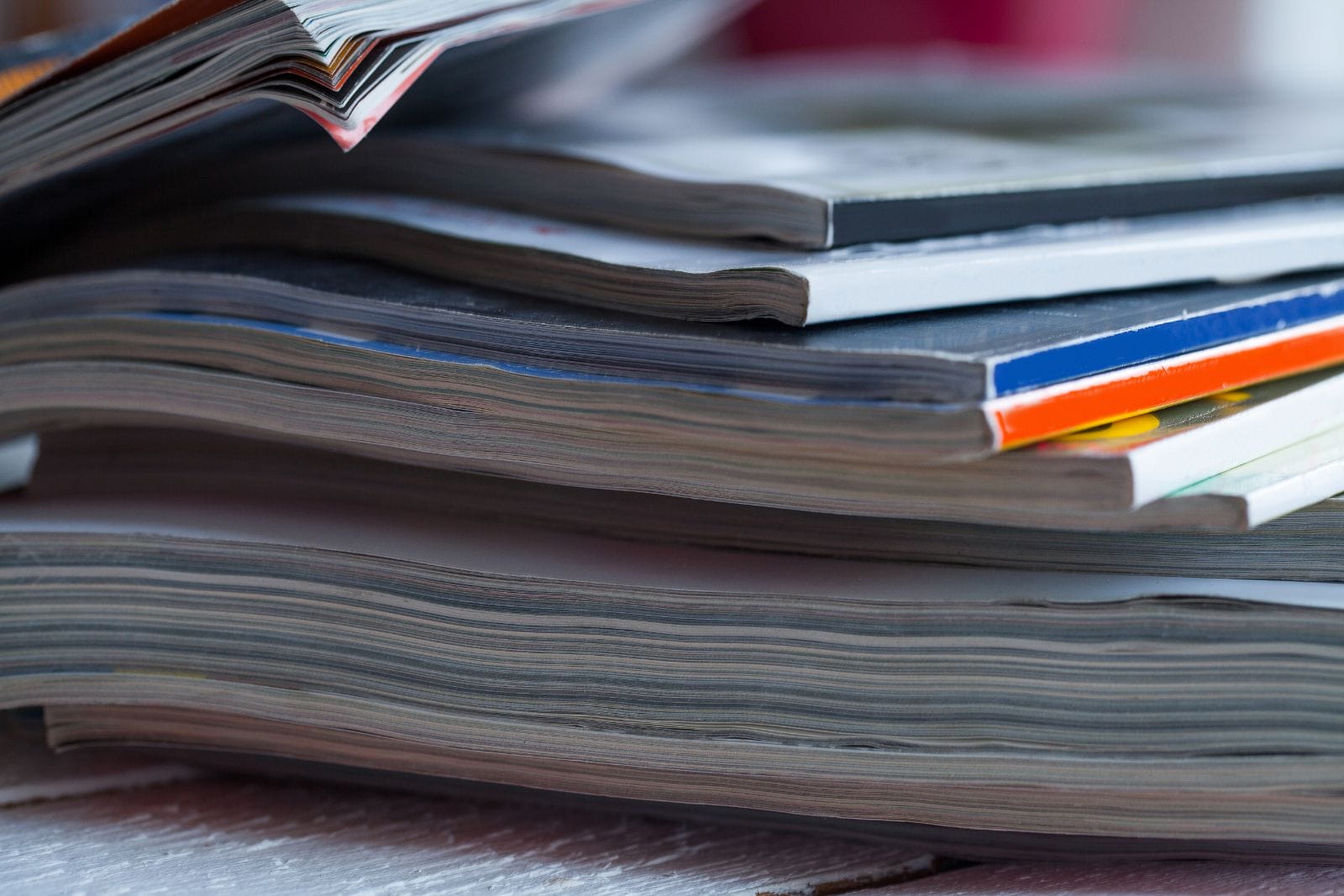 A close-up view of a stack of magazines and books, arranged unevenly on a surface.