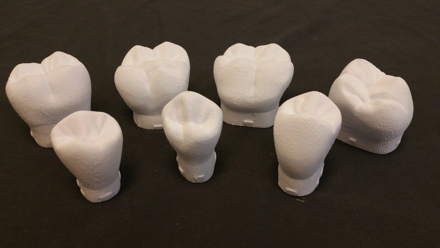 Seven white dental crown models are arranged on a black surface.
