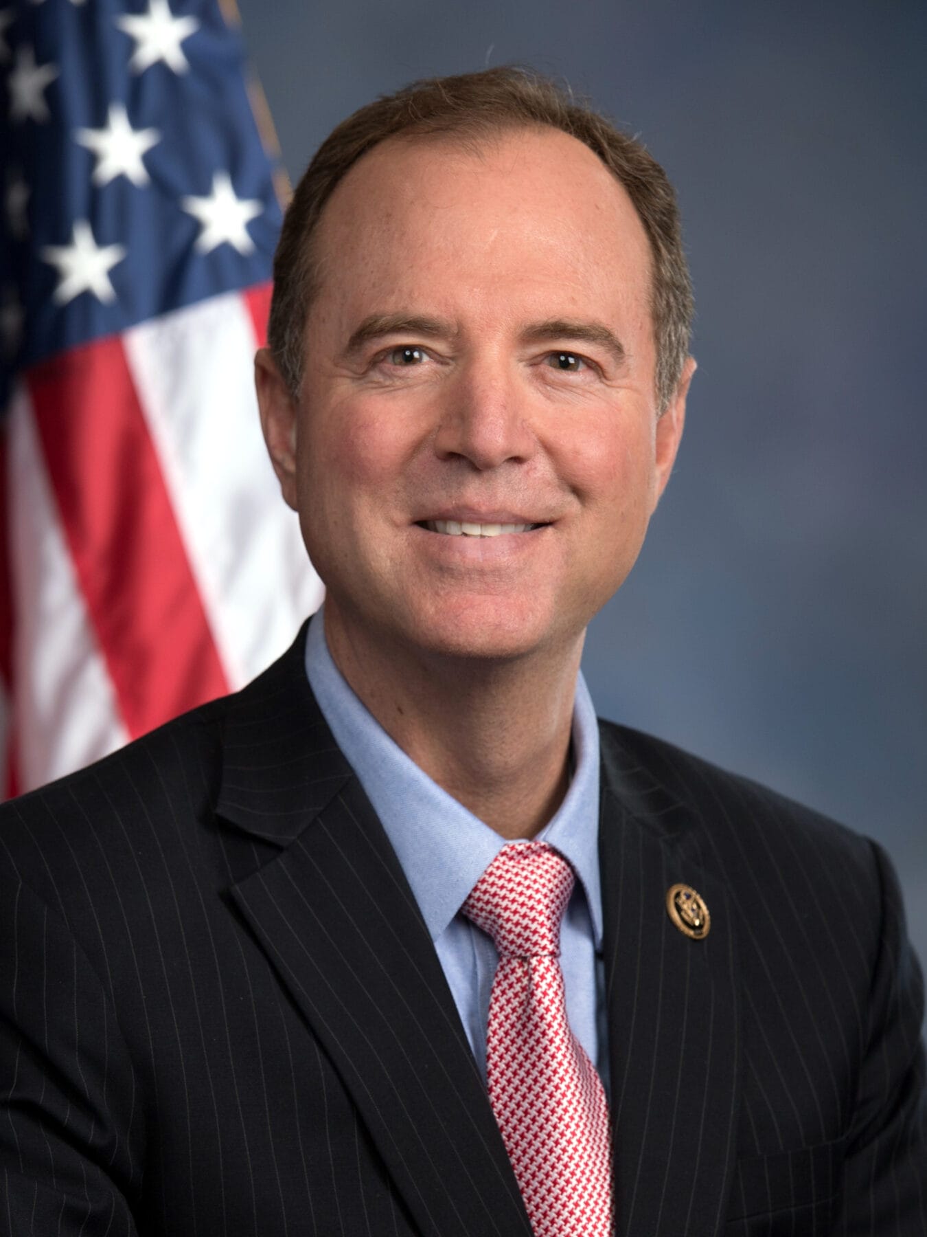 A person in a suit and tie poses in front of an American flag.