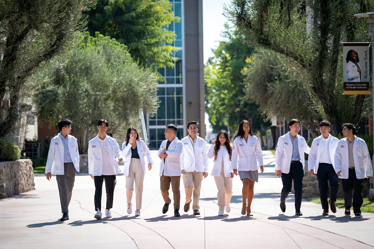 10 students in white coats walking down the esplande