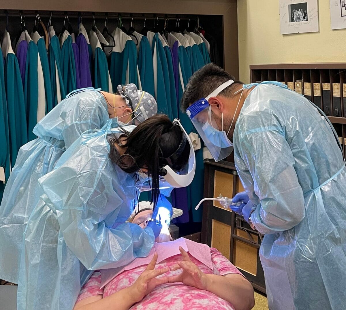 Three dental students working on patient in dental care clinic