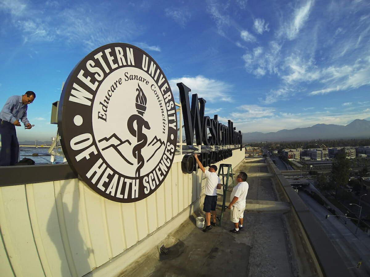 Two men are putting up a sign on the side of a building.