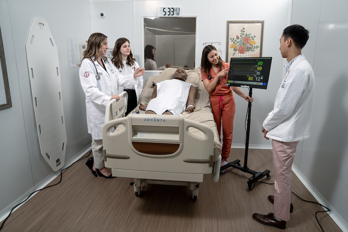 A group of people standing around a bed in a hospital room.