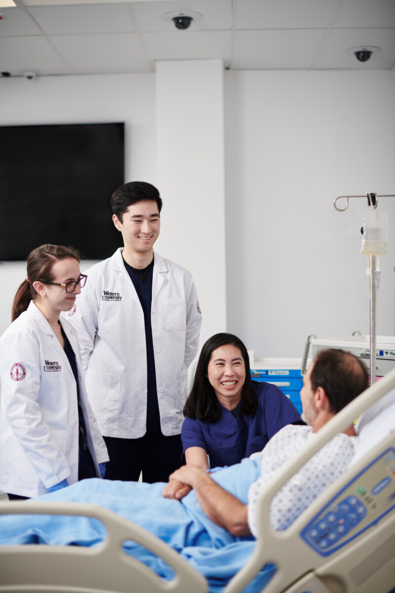 A group of medical students standing around a patient in a hospital bed.
