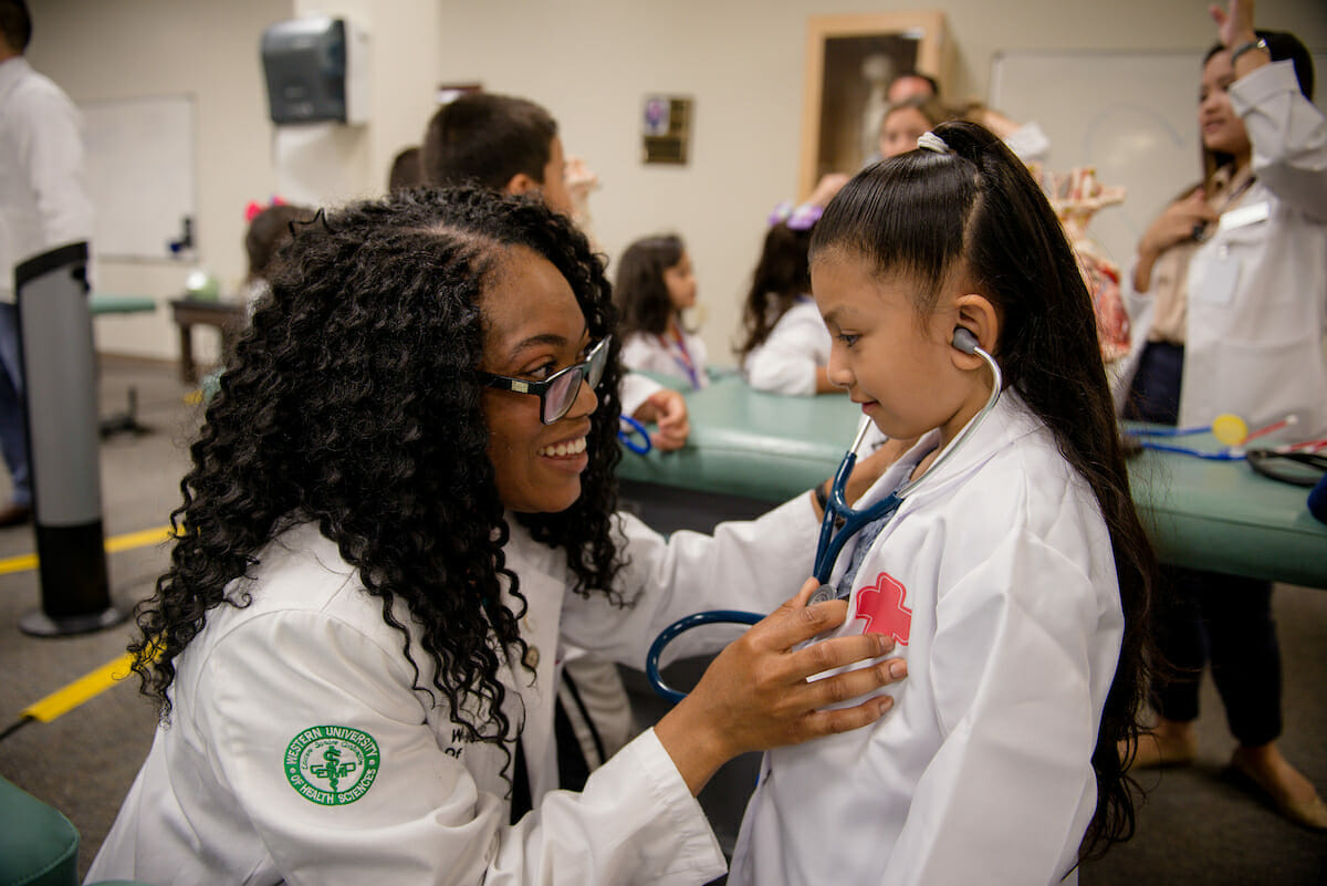 A young girl with a stethoscope in a classroom.