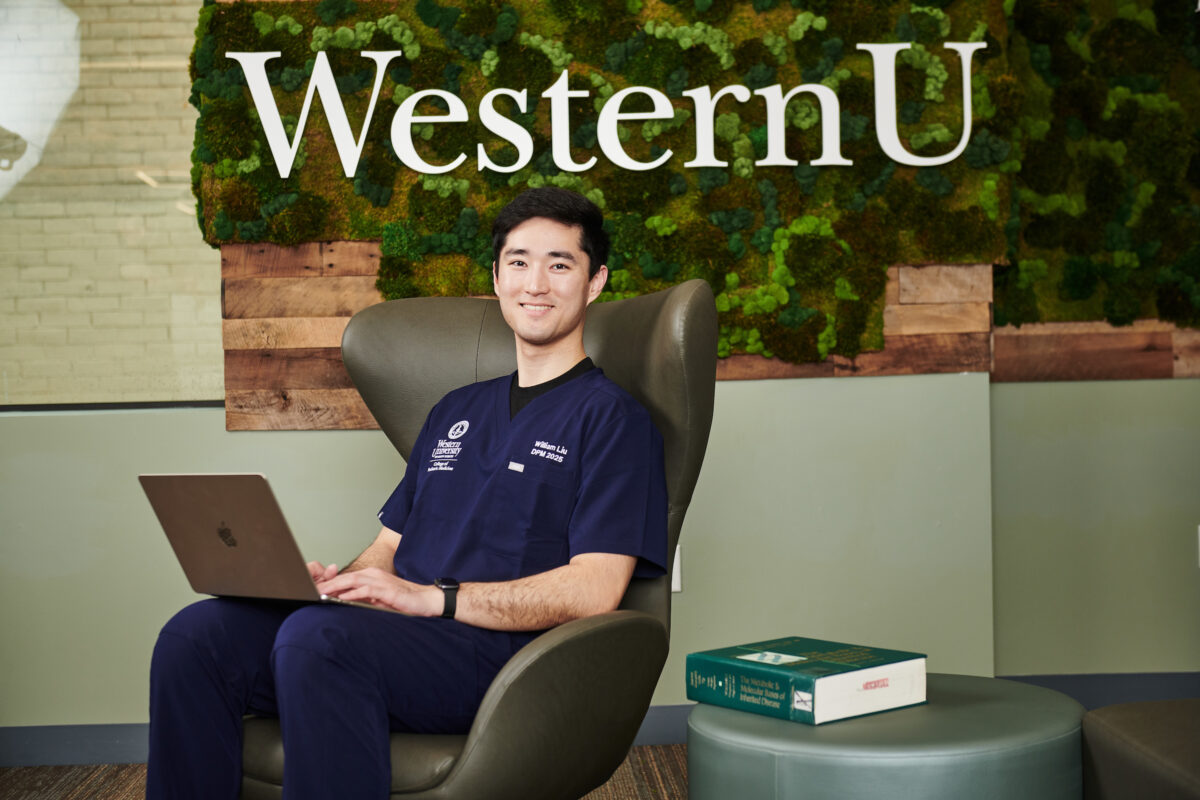 A man sitting in a chair with a laptop in front of a green wall.