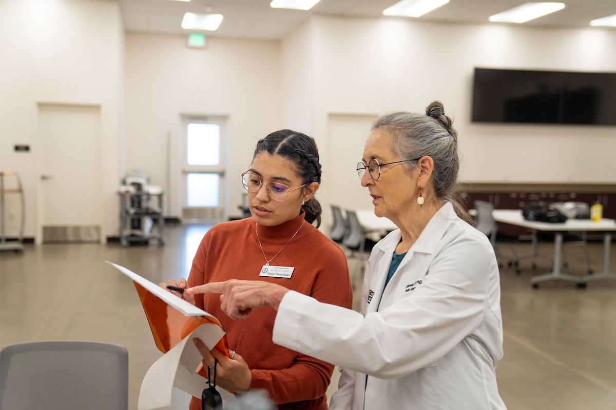 Two women in lab coats talking to each other.