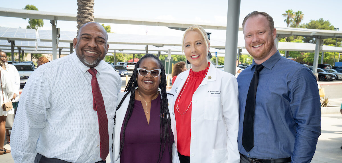 Four professionals posing together outdoors, two men and two women, with one woman in a medical lab coat.