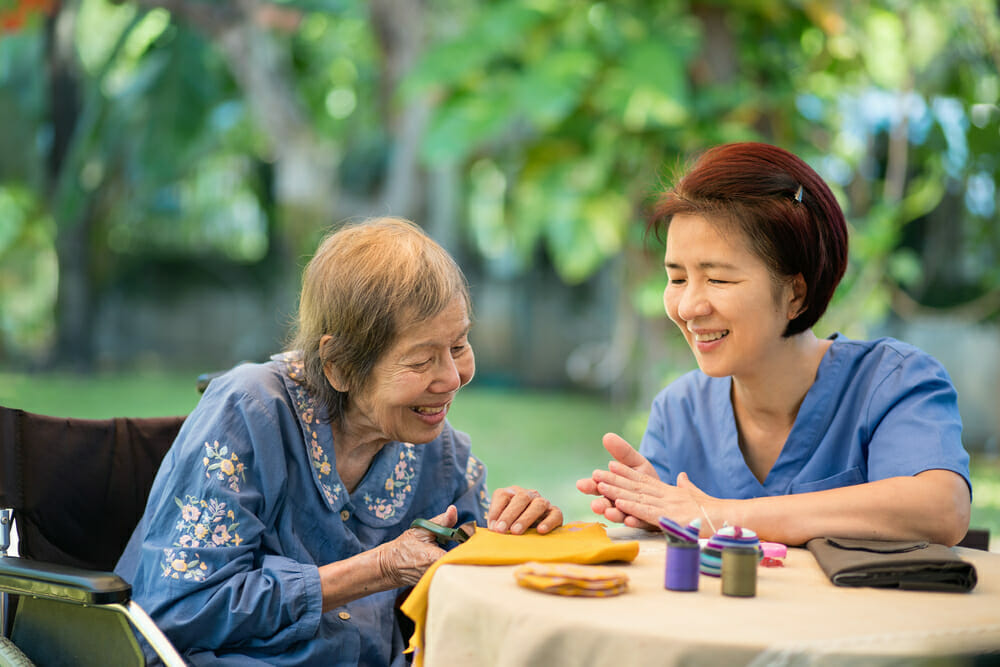 Two Asian women sitting at a table outdoors, cutting fabric