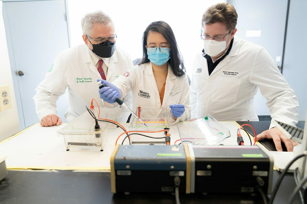 three people, lab coats, electronic equipment