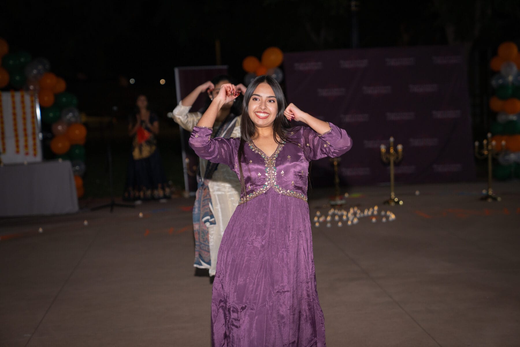 Person in a purple dress dancing outdoors at night, with balloons and others in the background.