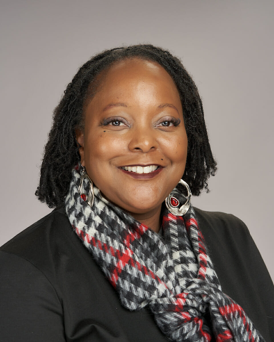 An african-american woman wearing a scarf and black jacket.