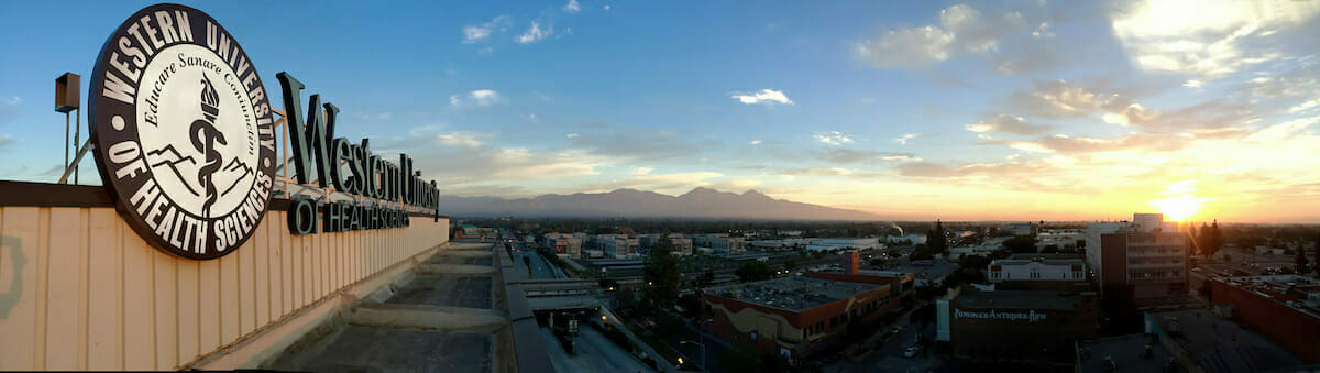The sun is setting over a city with a sign in the background.