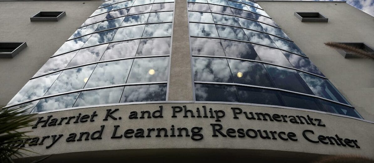 Glass facade of the Harriet K. and Philip Pumerantz Library and Learning Resource Center reflecting a partly cloudy sky.