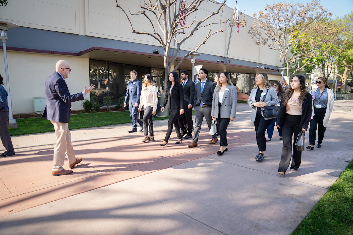 A group of professionals attentively listening to a man who appears to be giving a tour outside a building.