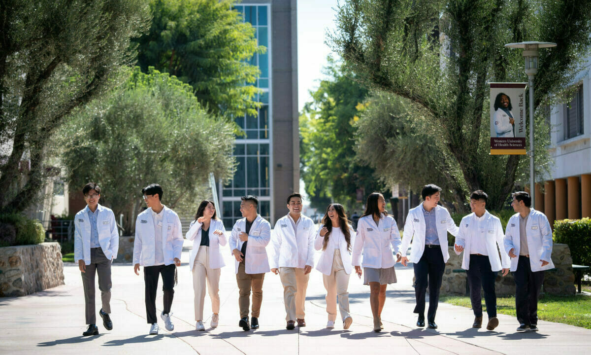 Students in white coats walking on California campus.