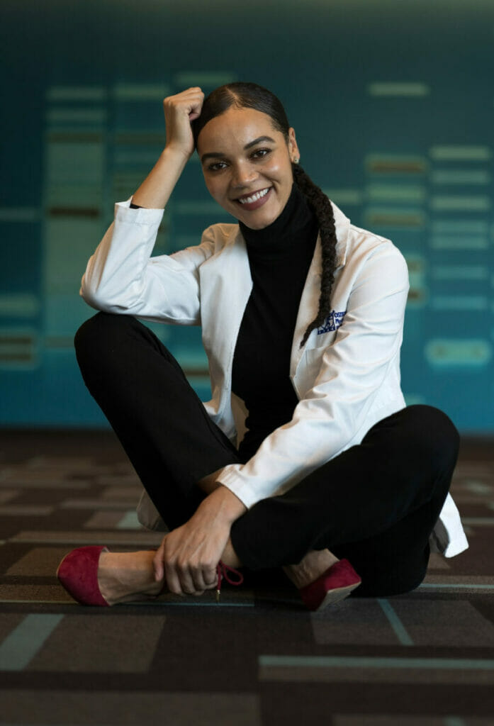 Azaria in front of DNA wall in WesternU's HEC building
