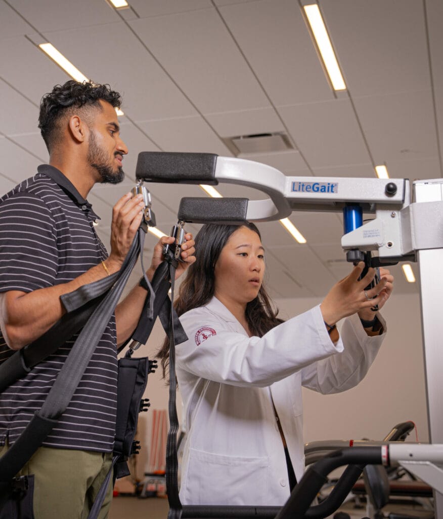 A therapist in a white coat assists a man using a LiteGait device in a clinical setting.