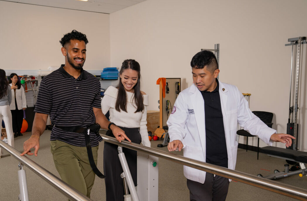 A physical therapist assisting a smiling man using parallel bars, with a woman observing them in a rehabilitation center.