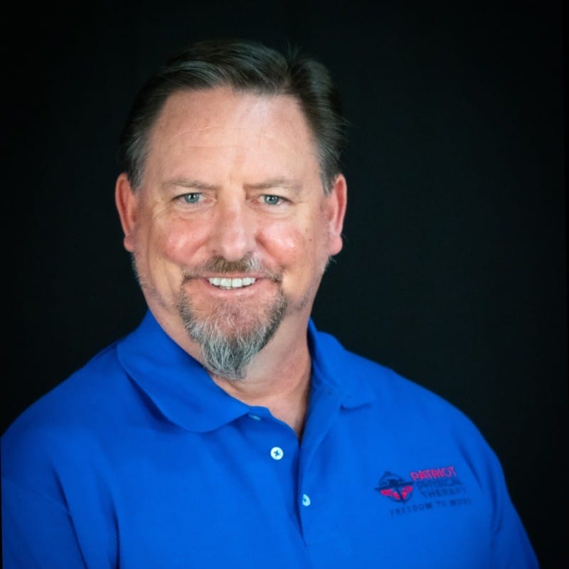Man with short hair and goatee, wearing a blue polo shirt, smiling in front of a black background.