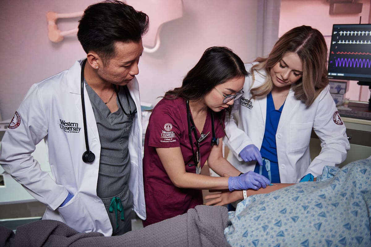Three healthcare professionals are examining a patient in a hospital setting, with medical equipment in the background.