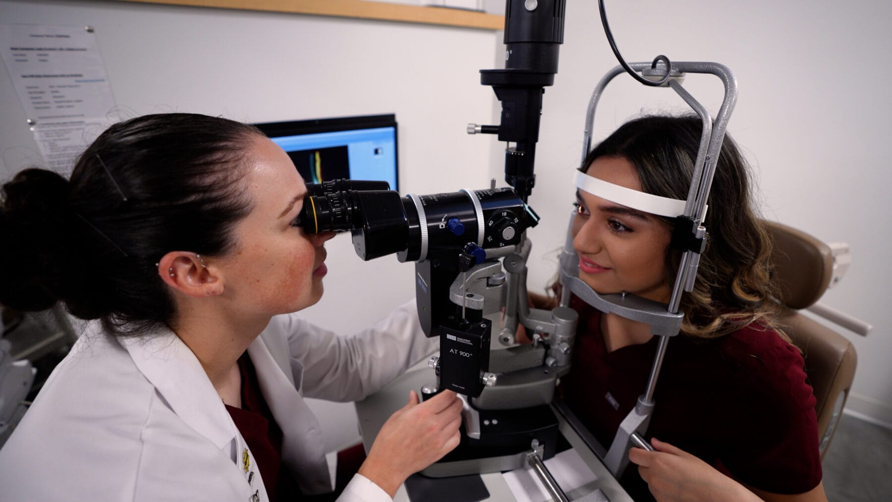 An optometrist examines a patient's eyes using a slit lamp machine in an eye care clinic.