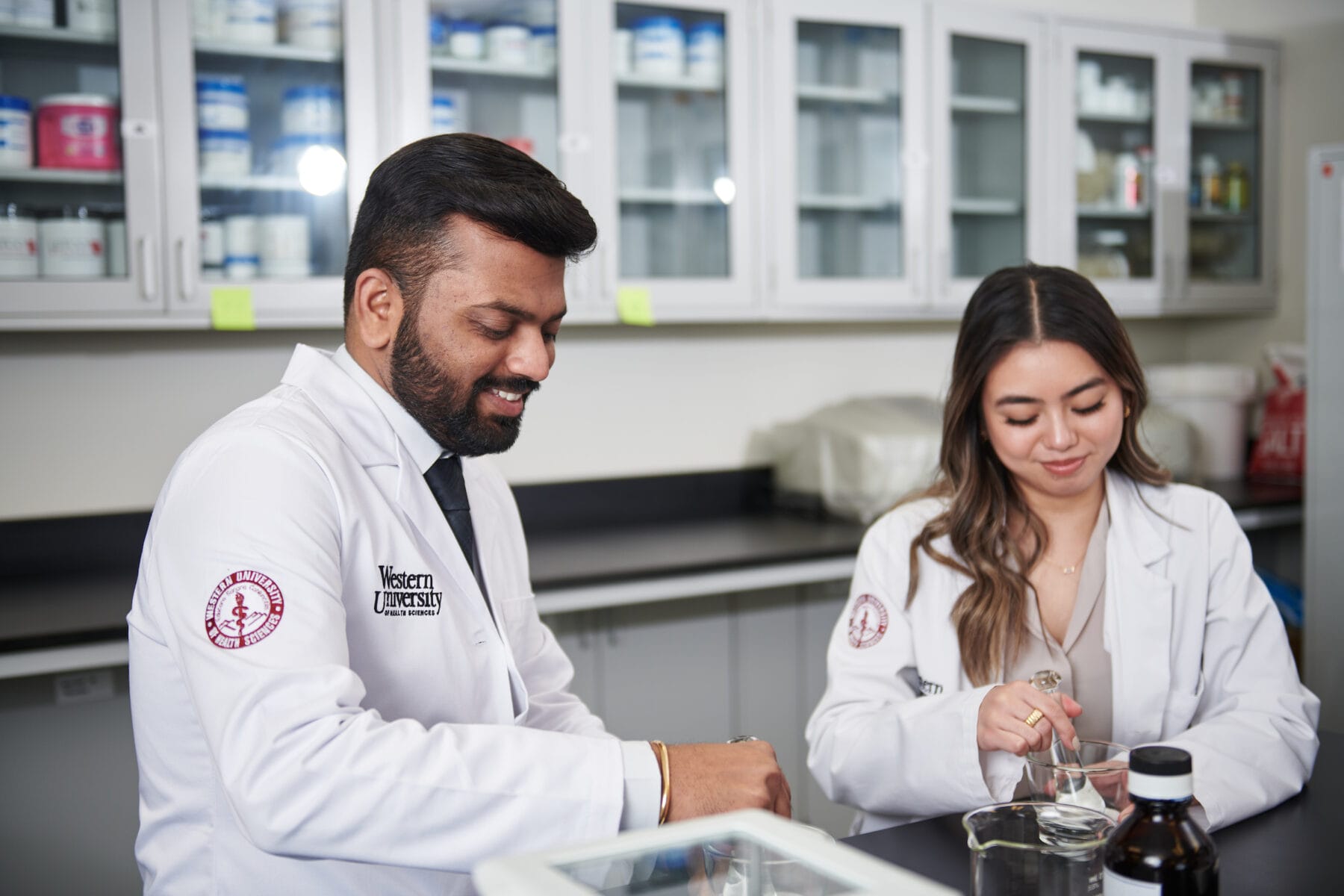 Two scientists in lab coats working together at a laboratory bench, using various equipment and materials.