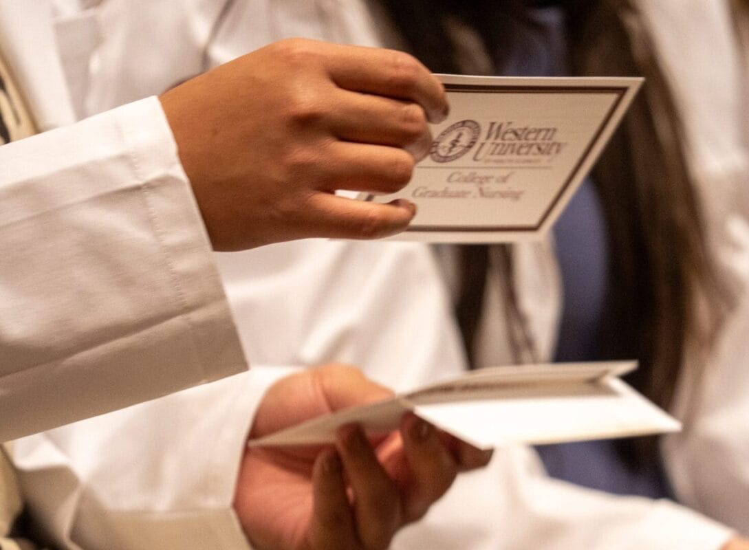 Person in white coat holds a card reading "Western University College of Graduate Nursing," during a ceremony.