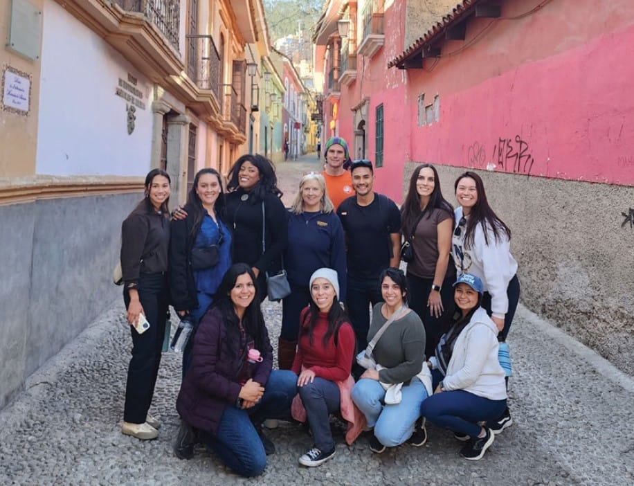 Group of people posing on a cobblestone street lined with colorful buildings in Bolivia.