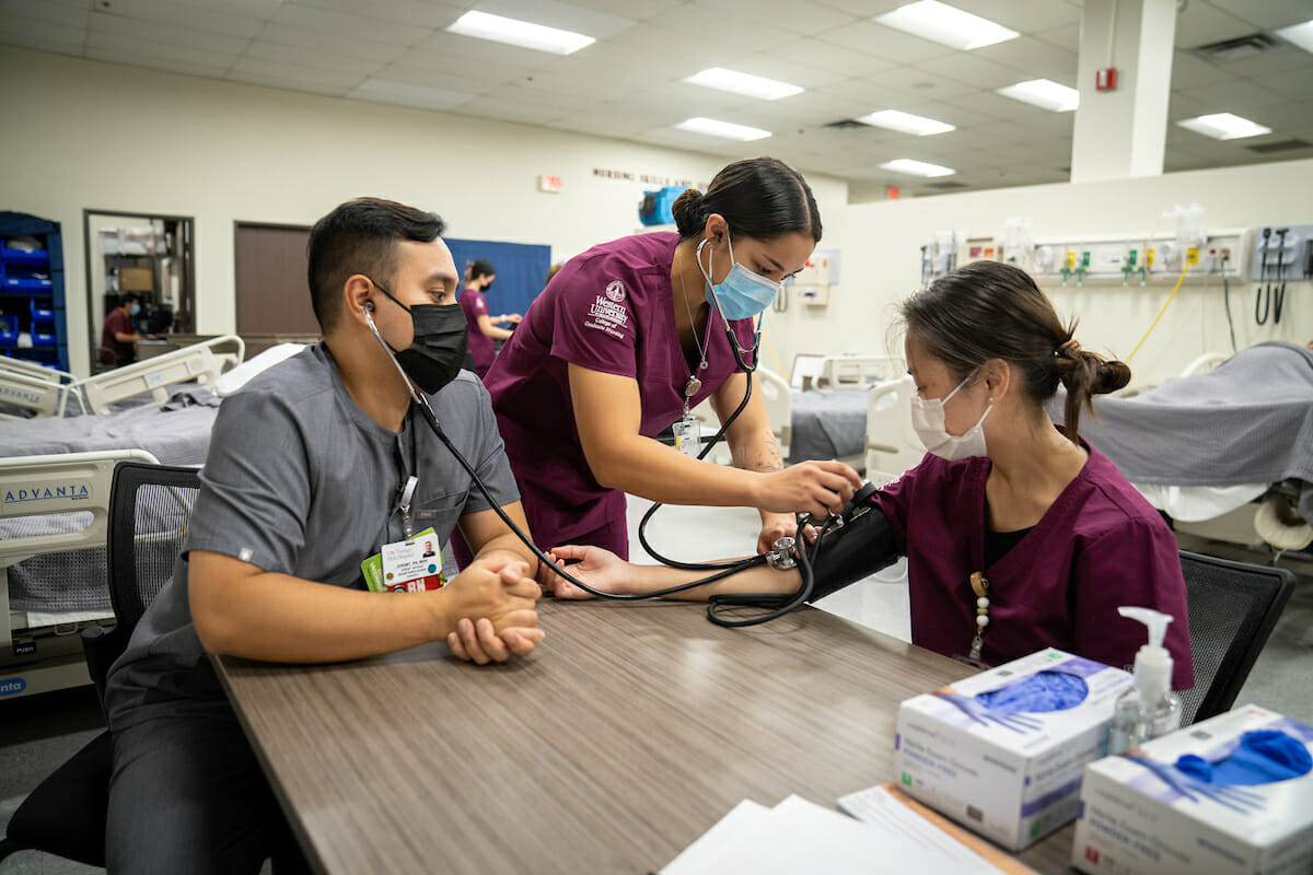 First-year MSN-E students participate in a midterm competencies and skills evealuation for Fall 2022. Jeremy Magana, RN, MSN, keeps a watchful eye on students Kaitlyn Parrish and Vy Nguyen.