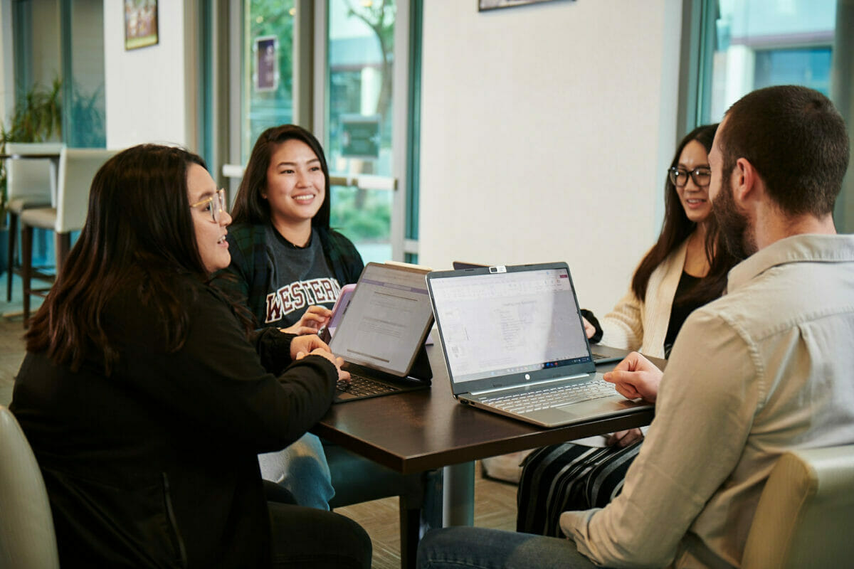 a group of students sitting around a table with a laptop.