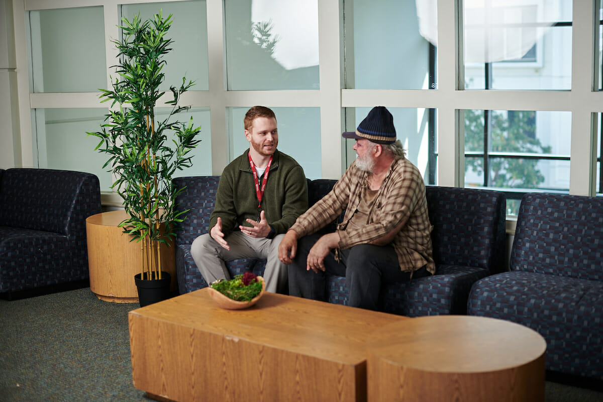 two men sitting on a couch talking to each other.