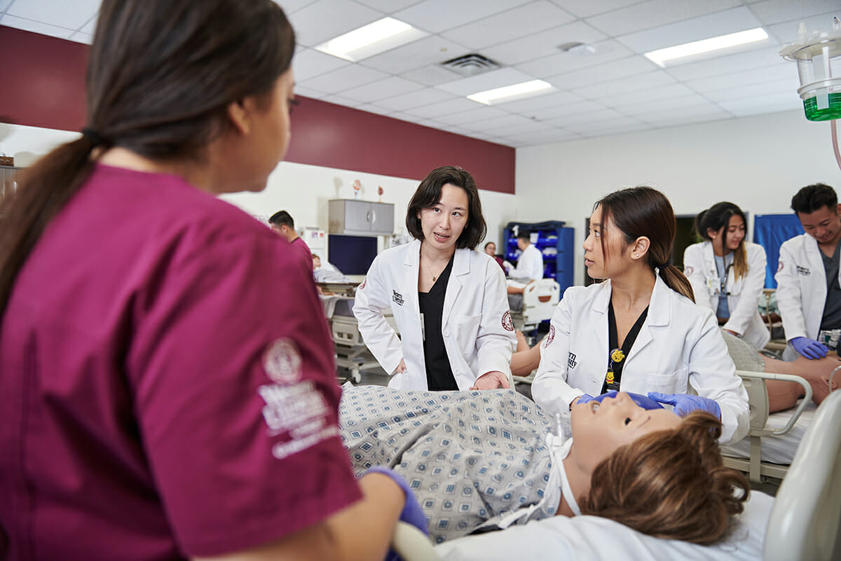 Two female nursing students with one female faculty member examining simulation mannequin.