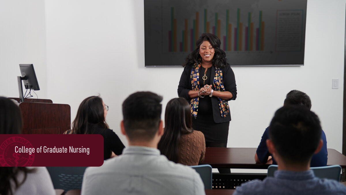 A female professor is teaching a diverse group of students in a classroom, standing in front of a digital graph display.