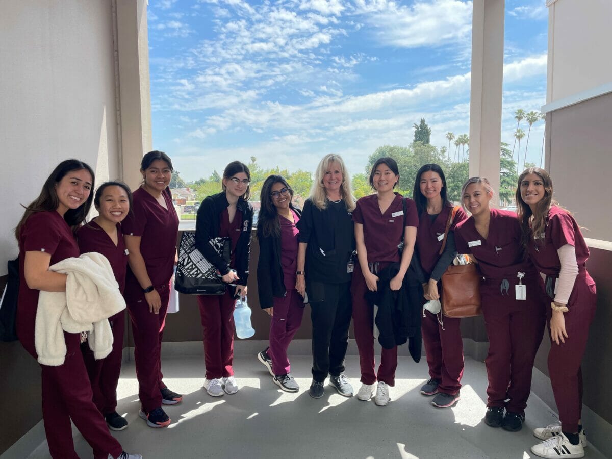 10 students in scrubs posing outdoors on balcony