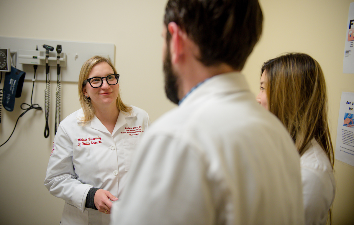 Two women in lab coats talking to a doctor.