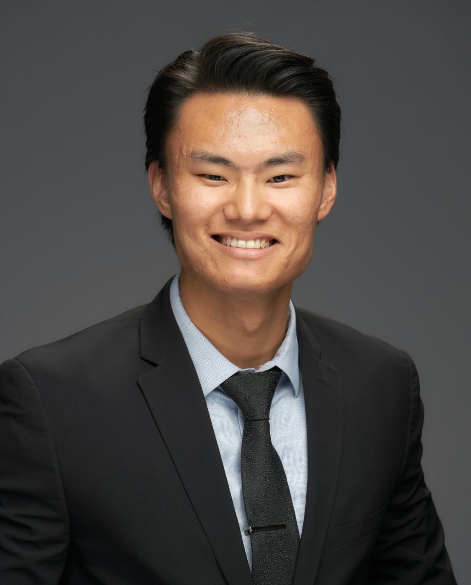 Asian man in a suit and tie smiling for the camera.