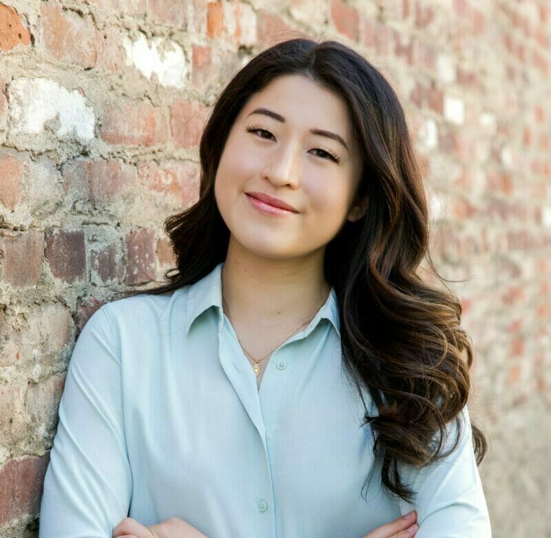 A young asian woman leaning against a brick wall.