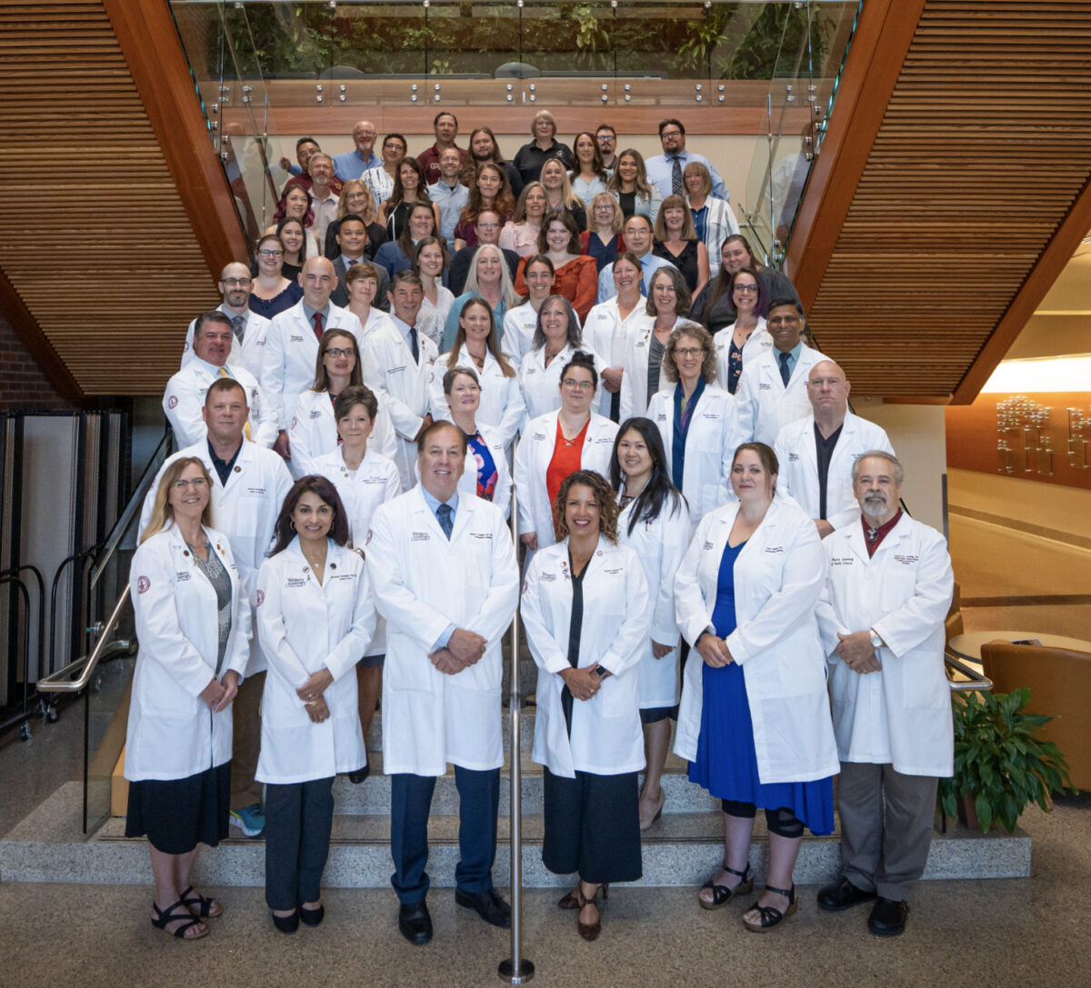 Group of medical professionals in white coats posing for a photo on tiered steps in a modern building.