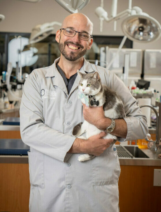 Veterinarian Kevin Ellis holding a cat in the PHC with medical equipment in the background.
