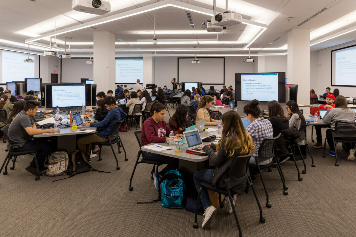 Students seated in classroom with multiple large screens displaying text