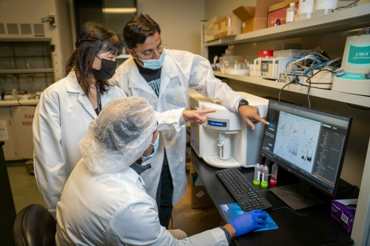 two people in lab coats looking at a computer screen.