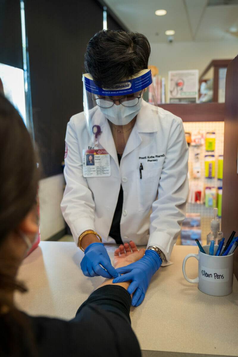 Doctor in white coat wearing protective face mask while tending to a patient at a pharmacy counter