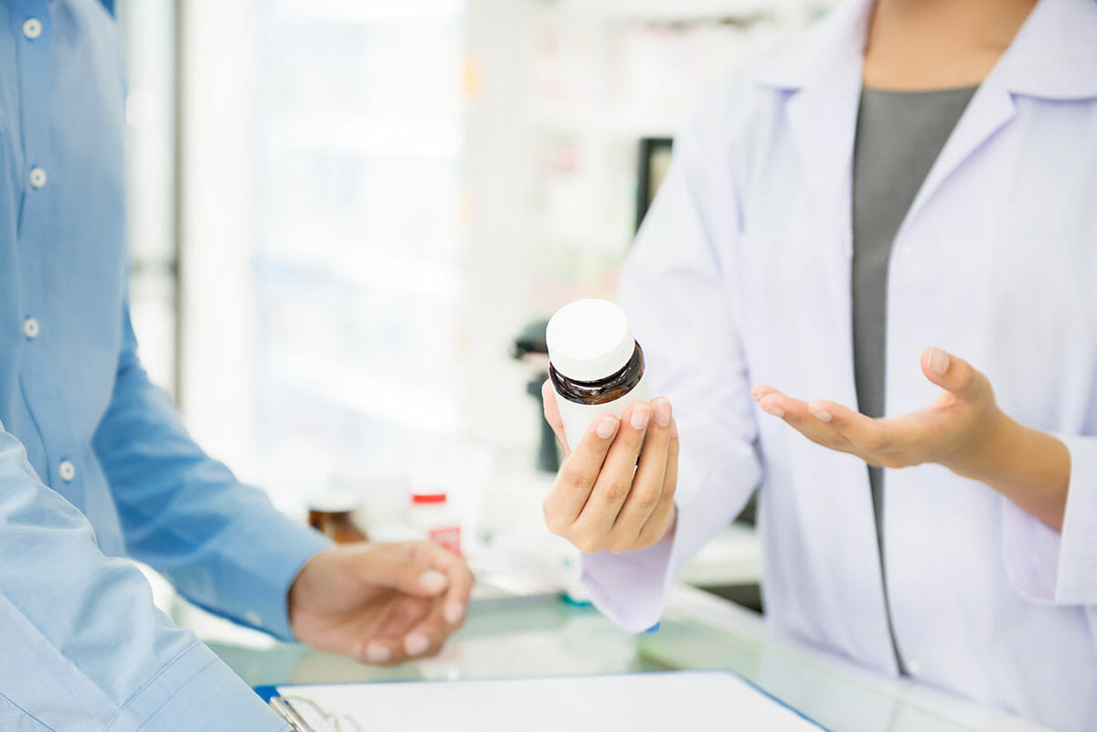 Image of hands of a pharmacist and a patient. Pharmacist is explaining to patient how to take medication.